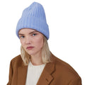 A person wears a Le Bonnet Large Beanie in light blue, paired with a brown coat, maintaining a neutral expression against a plain white background.