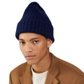 A person in a Large Beanie by Le Bonnet in navy blue and a brown coat over a white shirt against a white background exudes an aura of extreme comfort.