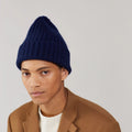 A person wears Le Bonnet's Midnight Beanie and a brown jacket over a cream sweater, looking at the camera against a plain background.