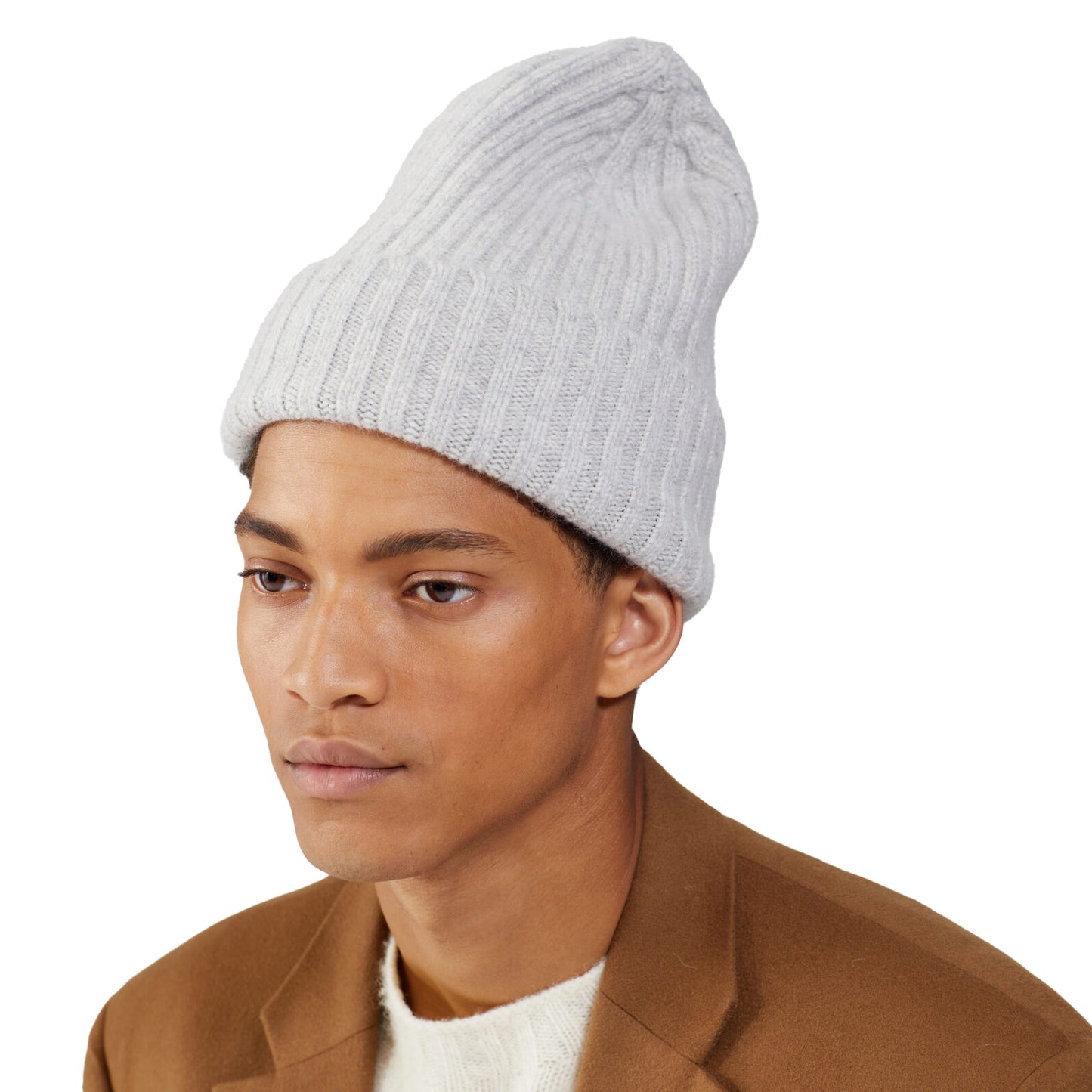 A person wears a Large Beanie by Le Bonnet in white knit with a brown coat, exuding extreme comfort while gazing to the side against a plain background.