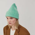 Wearing a Le Bonnet Beanie in Jade and a brown coat, a person gazes to the side against a plain background.