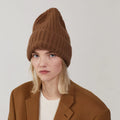 A person is wearing Le Bonnet's Large Beanie in Walnut, paired with a matching coat and white shirt designed for extreme comfort, standing against a plain background.