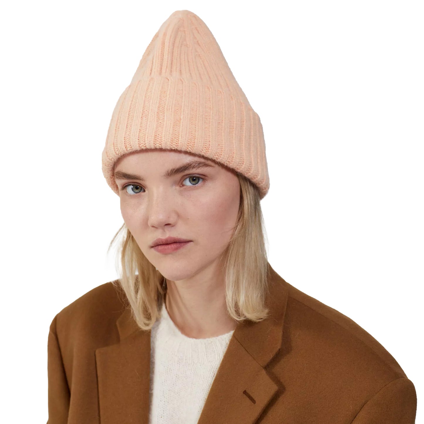 A person is wearing a Le Bonnet Large Beanie in peach for extreme comfort, paired with a cozy white sweater and a brown coat against a plain background.