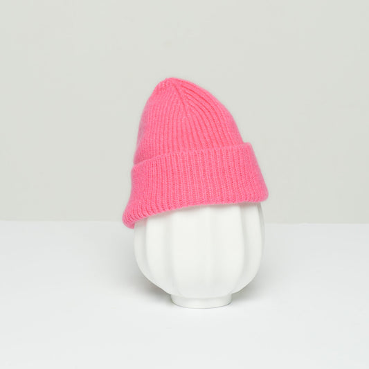 A white vase with a ridged texture is topped with Le Bonnet's K Beanie in Bubblegum, crafted from soft lambswool, against a plain background.