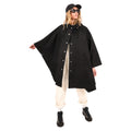 Someone wearing the Mackintosh W Boni, a black hooded poncho made from RAINTEC cotton, confidently stands with one arm extended. Sunglasses and a cap enhance their stylish look, while weatherproof clothing keeps them dry. Rolled-up light pants complete their striking ensemble.