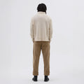 A person with dreadlocks wears the M's T Shape Roll Neck sweater by Margaret Howell and brown pants, standing with their back to the camera against a plain white background, evoking minimalist UK fashion vibes.