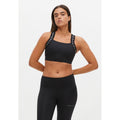 A person stands confidently in black athletic wear, featuring the Rohnisch Kay Sports Bra with branded straps and leggings made from sustainable recycled polyester. The sports bra boasts moisture-wicking properties. The individual has long, dark hair and a neutral expression.