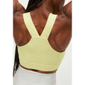 A person with dark braided hair is seen from behind, wearing the Kay Sports Bra by Rohnisch, which is made from light yellow recycled polyester and features a racerback design, paired with white leggings.