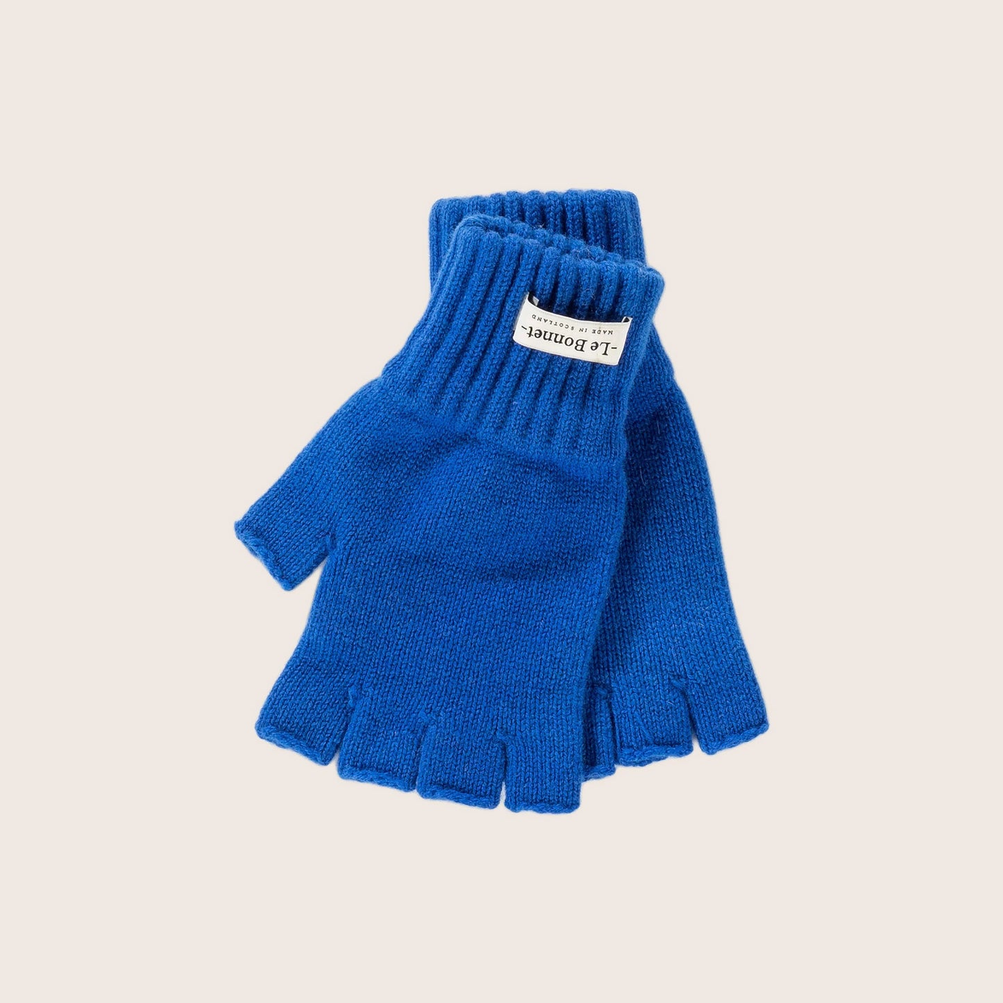 A pair of Le Bonnet's Royal Azure fingerless gloves, made from soft Merino wool and featuring a label, is presented on a plain background. Ideal for colder Scottish days when warmth and dexterity are needed.