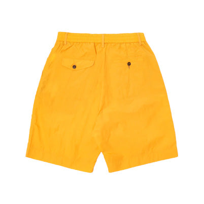 The Pleated Track Shorts by Universal Works, in orange, feature an elasticated waist with pleats and two back pockets with button closures, showcased against a white background.