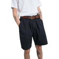 A person is wearing a white t-shirt, Universal Works Pleated Track Short in Dark Navy, and a brown belt, with their hands in pockets and tattoos visible on their forearms.