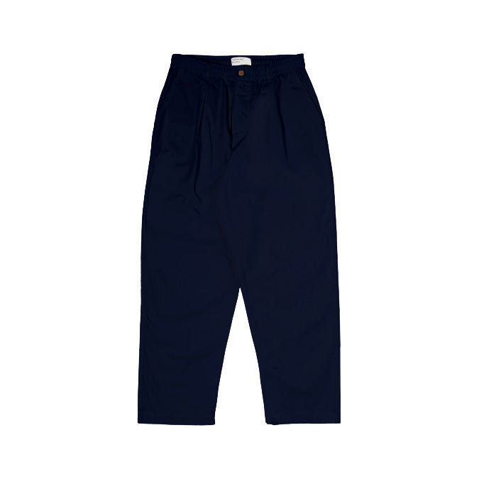 The Oxford Pant in Navy by Universal Works is a dark blue high-waisted trouser with a single pleat and button closure, elegantly displayed on a white background.