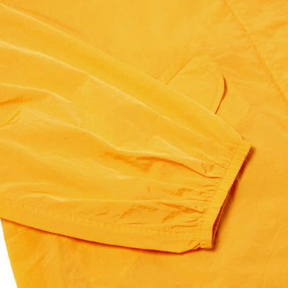 Close-up of a BEACH PARKA sleeve by Universal Works in orange, featuring an elastic cuff and a visible pocket.