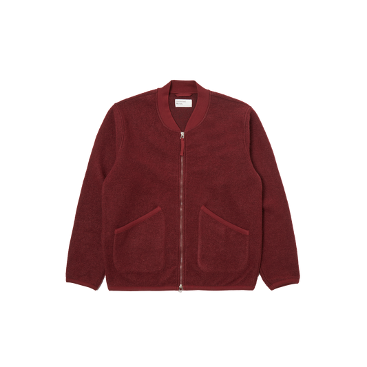 Universal Works introduces the Zip Bomber Fleece, a red jacket designed with a two-way zip and a simple collar. It is crafted in a regular fit and includes two front pockets for practicality.