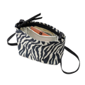 A Zipper Pouch Mini by Bags in Progress, designed with a zebra print and made from recycled polyester, is open to reveal a book, cash, and an envelope inside.