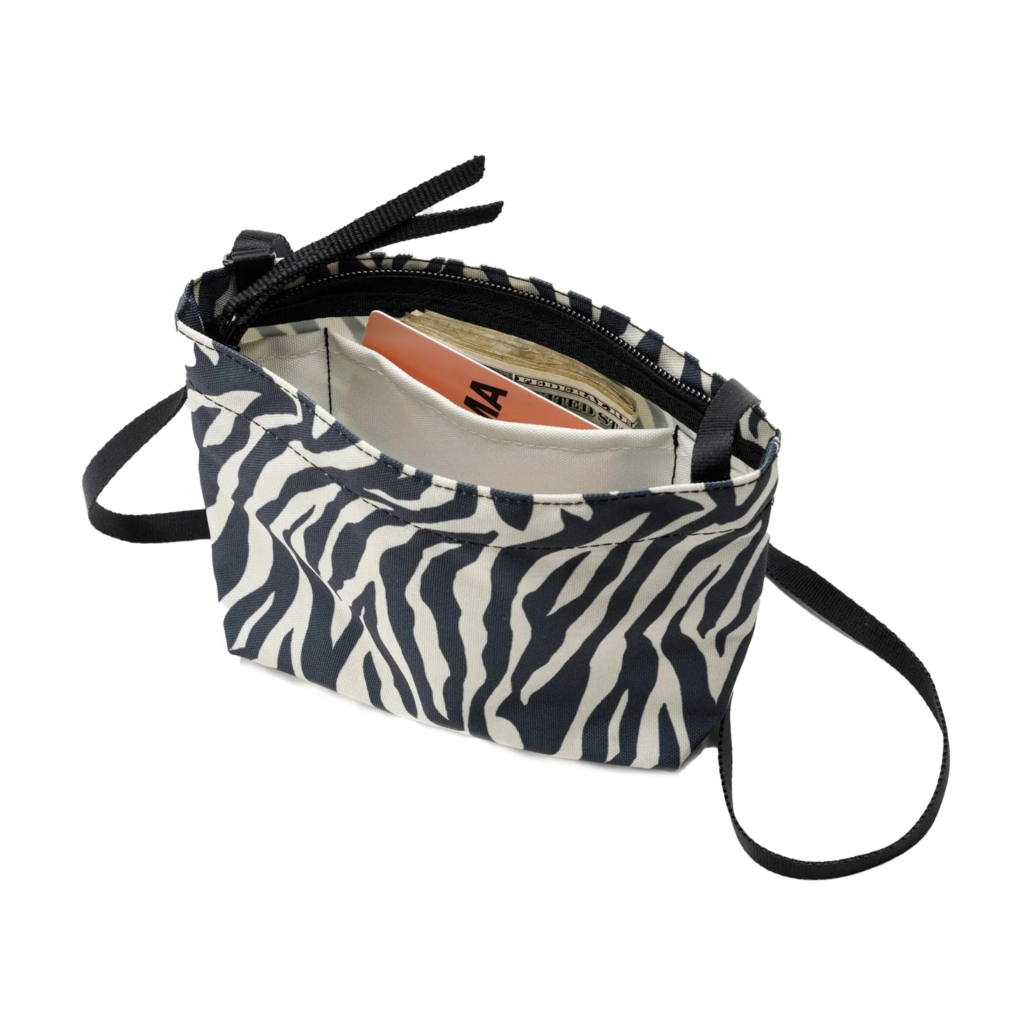 A Zipper Pouch Mini by Bags in Progress, designed with a zebra print and made from recycled polyester, is open to reveal a book, cash, and an envelope inside.