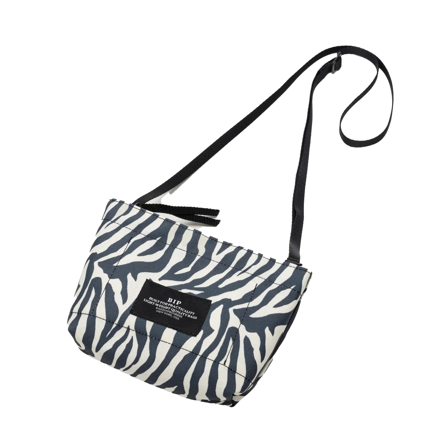 The Zipper Pouch Mini by Bags in Progress is displayed against a plain background, featuring a zebra pattern, black strap, and a rectangular black label on the front. Made from recycled polyester, this fashionable accessory also offers water-repellent features for enhanced durability.