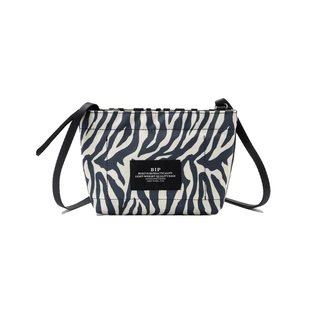 Introducing the Zipper Pouch Mini by Bags in Progress, a stylish shoulder bag featuring a zebra-print design crafted from recycled polyester. It is accented with black drawstrings and includes a label on the front.